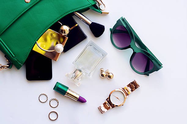 Top view of female fashion accessories . Green hanbag with sunglasses, gold watch , lipstick , perfume , rings , smartphone